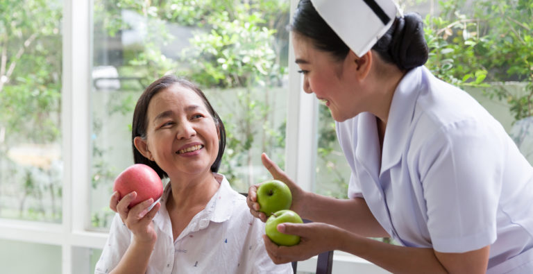 Nurse taking care or recommend senior Asian woman eating apple or fruit at home. Nurse assistant careful elderly Asian woman with kindly. Retirement, health care and ageing concept