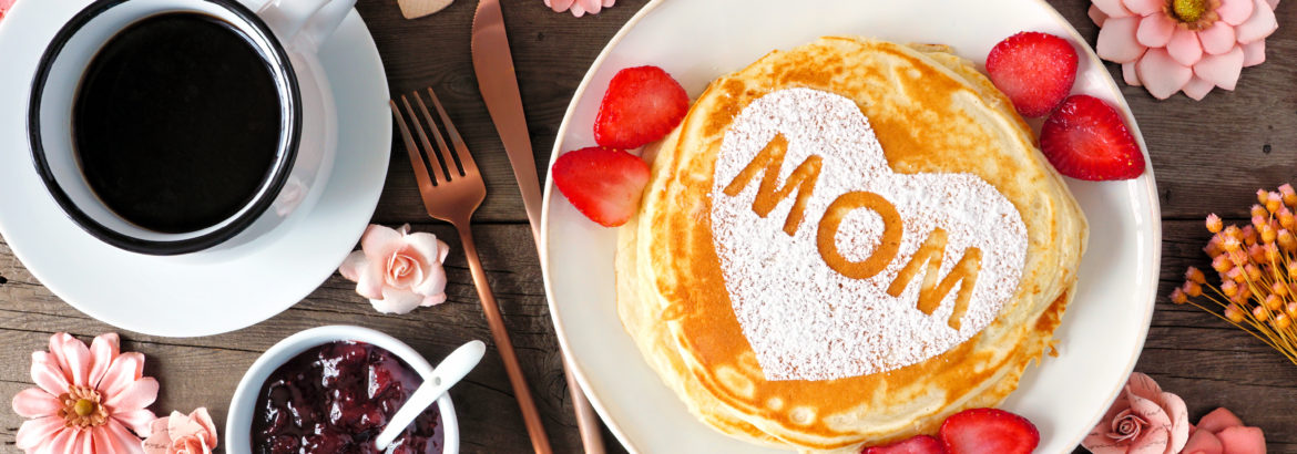 Mothers Day breakfast pancakes with heart shape and MOM letters, overhead view table scene on rustic wood