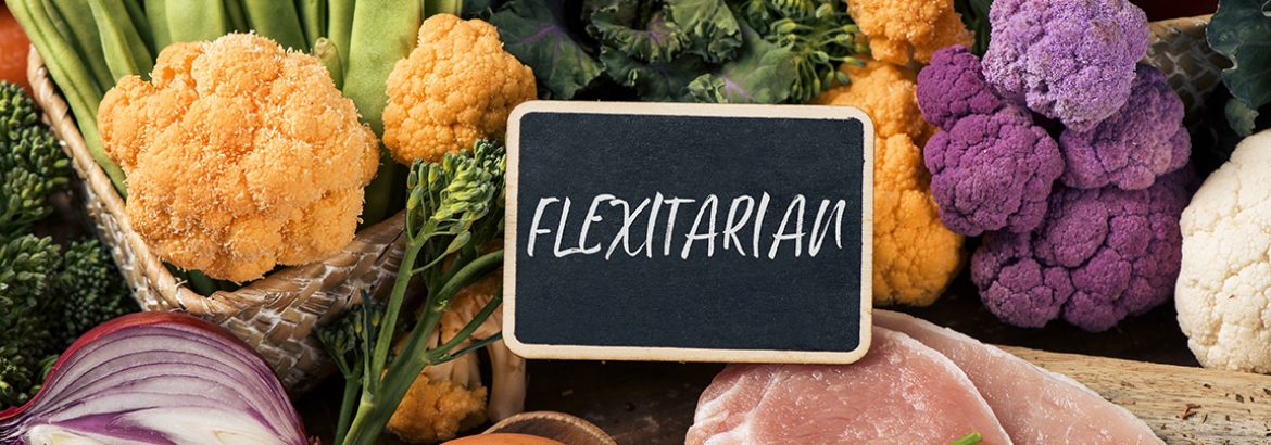 closeup of a signboard with the text flexitarian on a pile of some different raw vegetables, such as cauliflower of different colors, broccolini, or french beans, and some eggs and slices of meat
