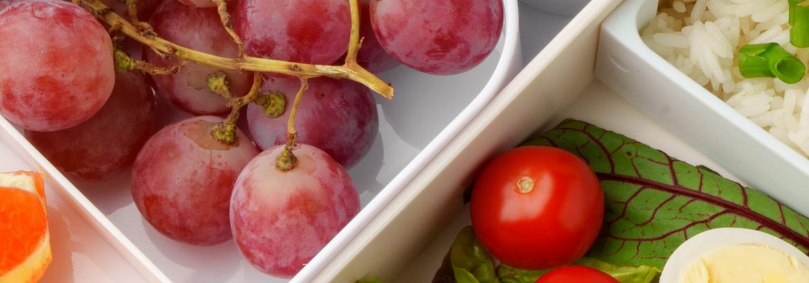 Lunch box shows various fruits, vegetables, and rice in organized sections for a healthy meal.