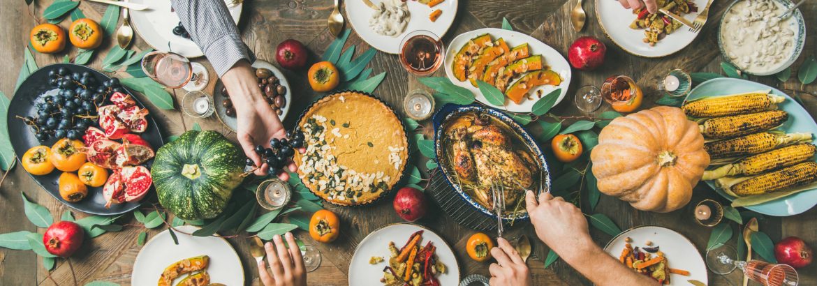 Thanksgiving, Friendsgiving holiday celebration. Flat-lay of friends feasting at Thanksgiving Day table with turkey, pumpkin pie, roasted vegetables, fruit, rose wine, top view