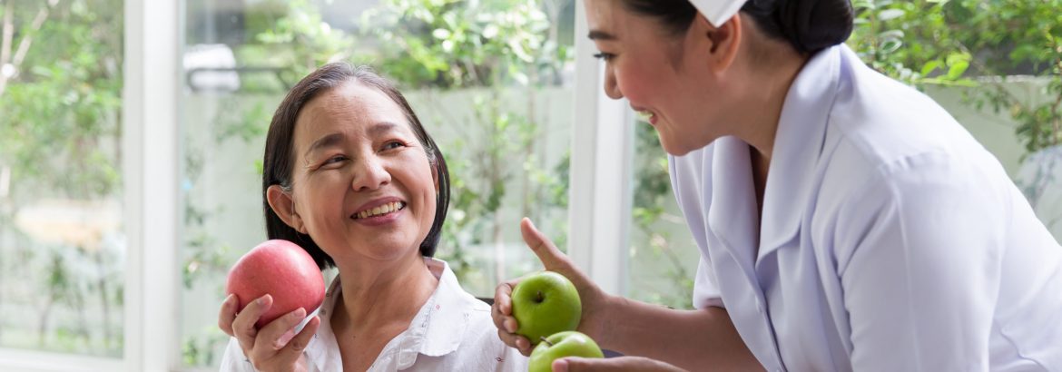 Nurse taking care or recommend senior Asian woman eating apple or fruit at home. Nurse assistant careful elderly Asian woman with kindly. Retirement, health care and ageing concept