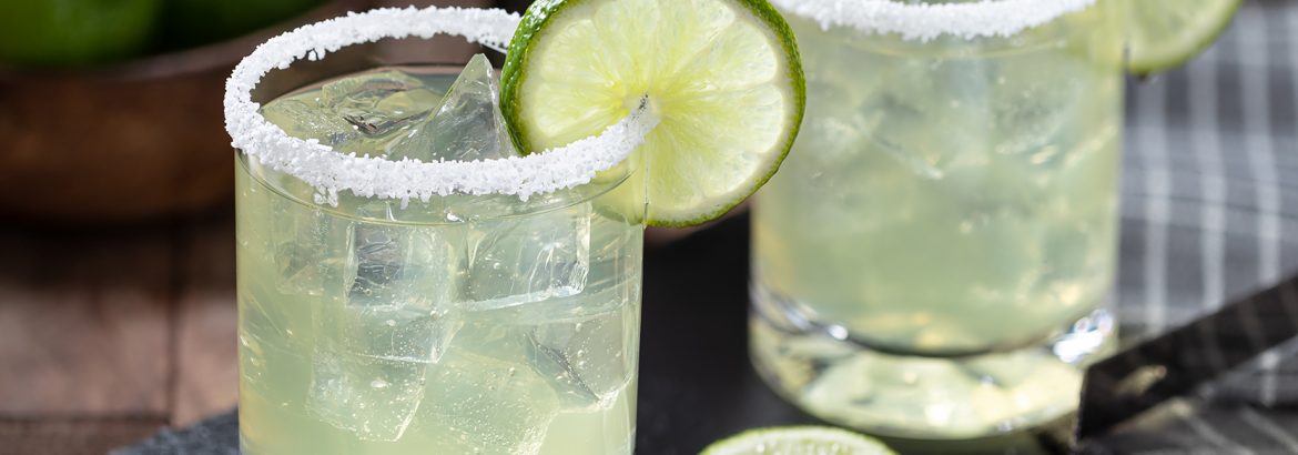 Margarita cocktail with ice, lime slice and salt rim on a black slate board