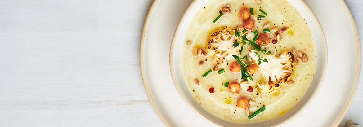 Healthy vegan cauliflower soup served in bowl on white table.