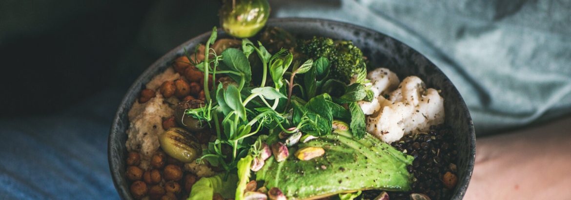 Healthy dinner or lunch. Woman in t-shirt and jeans sitting and eating vegan championship game or Buddha bowl with hummus, vegetable, fresh salad, beans, couscous and avocado