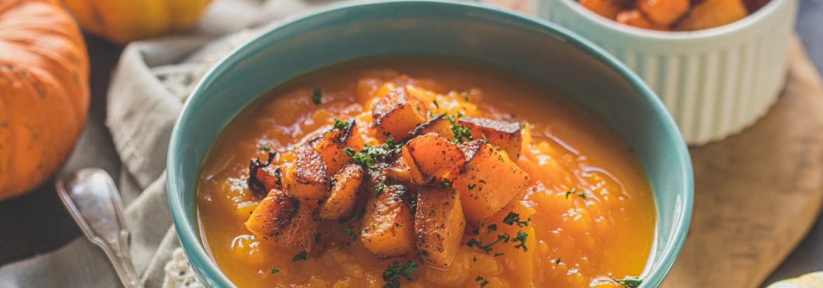 Homemade pumpkin cream soup with baked pumpkin pieces and parsley in a blue bowl