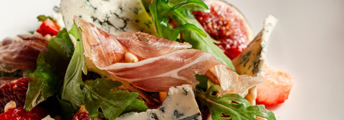 Salad with hamon ham, figs, blue cheese, arugula and strawberry on a plate. Dark Wooden background.