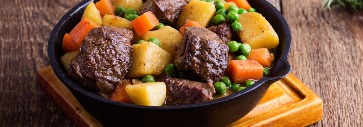 Beef and vegetable stew with potatoes in cast iron skillet on rural table