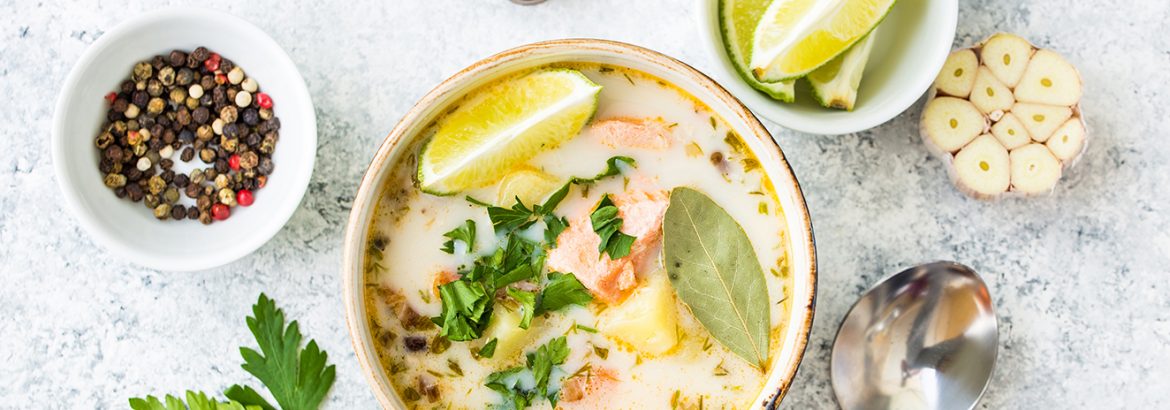 Salmon soup with potatoes, carrot, cream, herbs. Scandinavian/Norwegian fish soup in bowl, cutting wooden board, spoon, rustic white concrete background. Salmon soup for dinner. Top view. Close-up