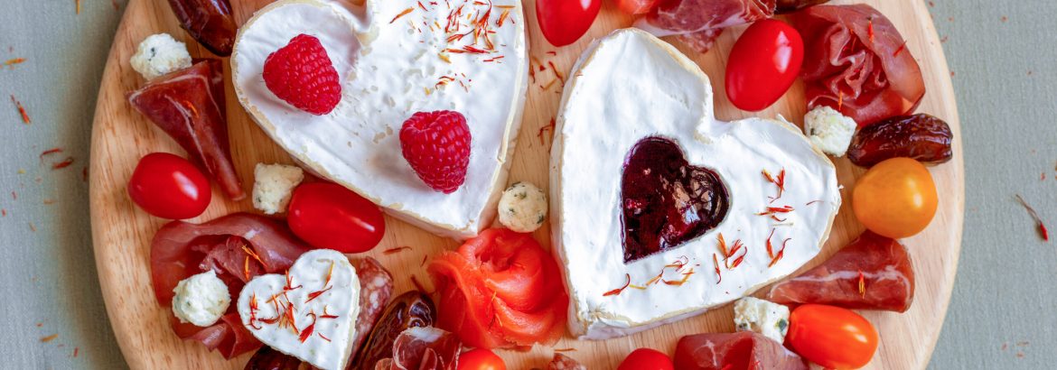 cheese plate with heart shape cheese, fruits and delicatessen, decorated with edible flowers