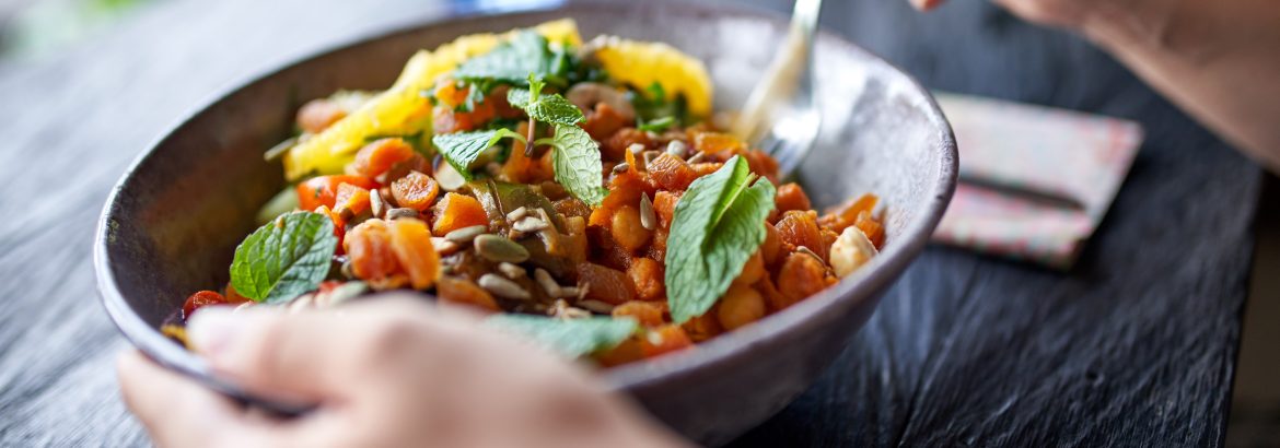 Closeup shot of vegetarian person hands holding gourmet championship game lunch dish with chickpeas mint, fresh herbs and fruit at wooden table drinking organic fair-trade coffee