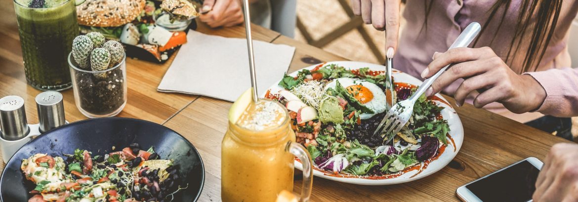 Hands view of young people eating brunch and drinking smoothies bowl with ecological straws in plastic free restaurant - Healthy lifestyle, food trends concept - Focus on top fork dish