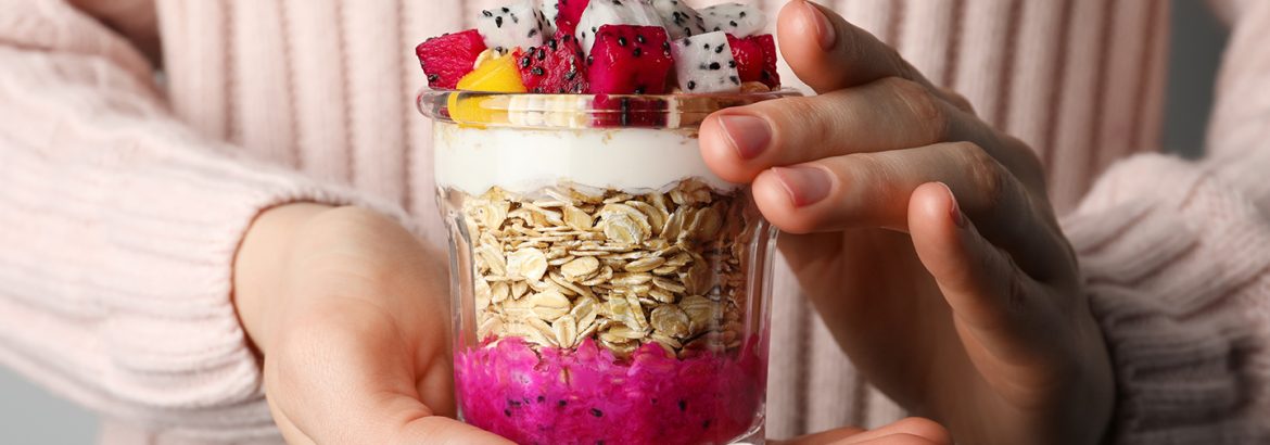 Woman holding glass of granola with pitahaya, yogurt and mango, closeup