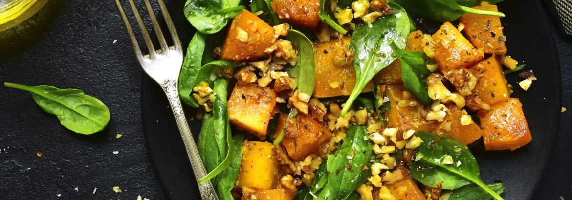 Roasted pumpkin salad with spinach and walnut on a black plate on a stone background.Top view.