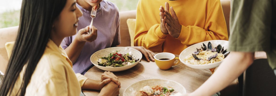 Customers enjoying a meal in a modern cafe, chatting happily. A diverse group of friends sharing salads and pasta, with natural light streaming in