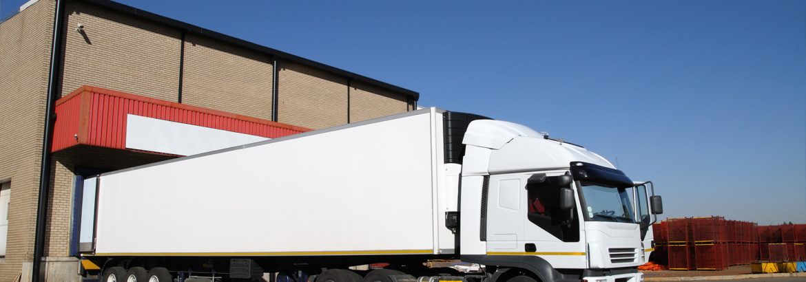 Refrigerated semi truck at a cold storage warehouse loading bay.